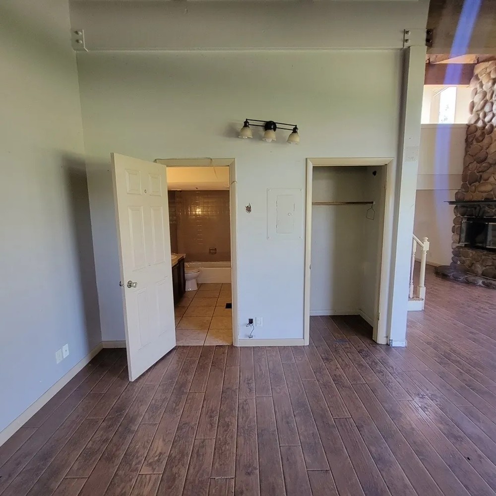 Before: a finished Park City bedroom with painted drywall walls, wood-plank flooring, an open doorway to a tiled bathroom and a closet opening